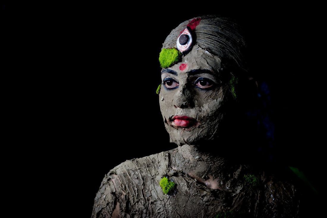 Woman demonstrating how to use clay mask properly by applying a green clay paste to her face with a brush.