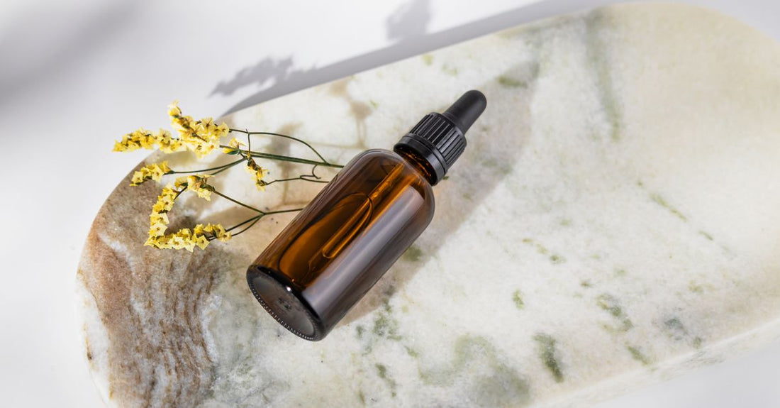 Clear glass bottle of tanning drops on a white marble surface.