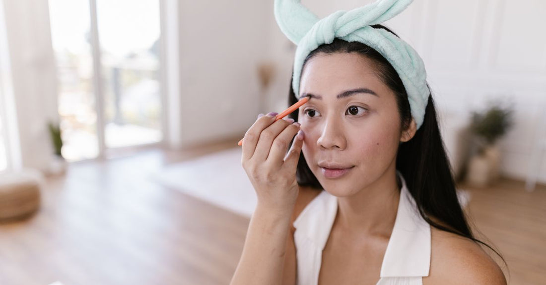 A selection of the best eyebrow products for sparse brows, including a precise eyebrow pencil, a nourishing growth serum, and a brow stamp kit, arranged on a clean marble surface.