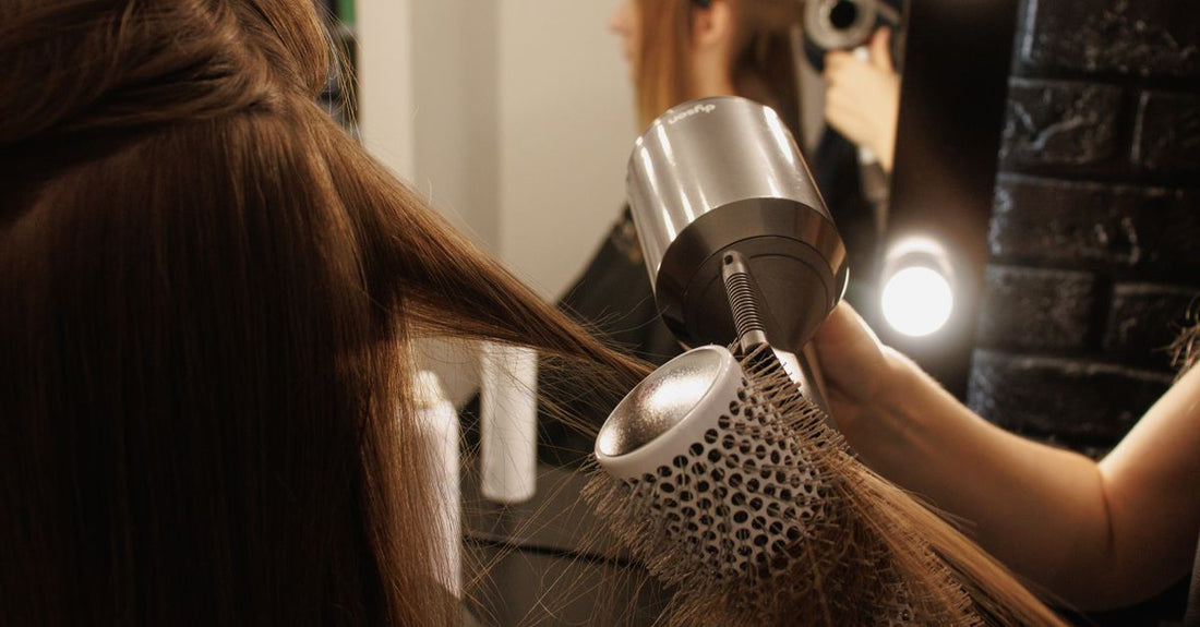 A black universal hair diffuser attachment for curl definition, photographed on a light background with a hairdryer nozzle visible in soft focus.