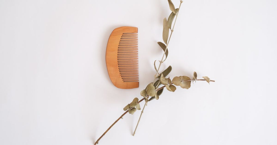 A wooden beard comb and boar bristle brush on a neutral flatlay surface, demonstrating how to choose beard & mustache combs for effective grooming.