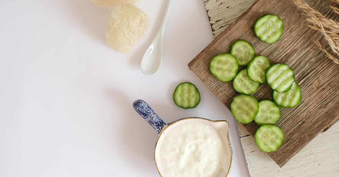 Natural ingredients for reducing dark circles: cucumber slices, almond oil, and cold tea bags on a marble surface.