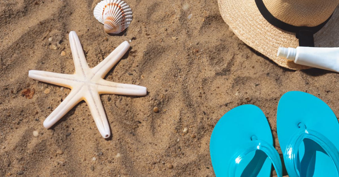 A row of body sunscreen bottles on a sandy surface, representing a body sunscreens buying guide for UK shoppers.