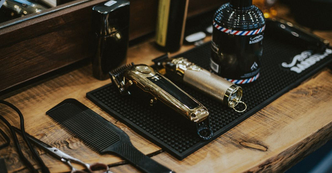 A pair of professional hair clippers resting on a white tabletop next to a comb and clipper guards, illustrating how to cut your own hair with clippers at home.
