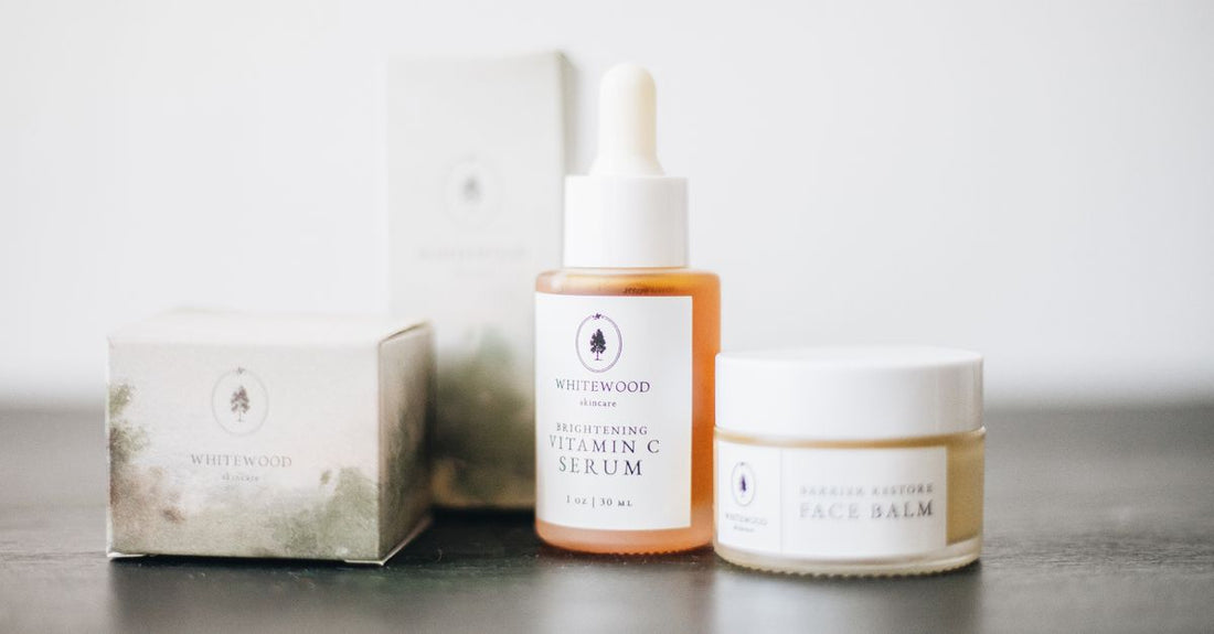 Three small glass jars of Frøya Organics anti-aging routine balms on a marble surface with fresh rosehip and sea buckthorn berries.