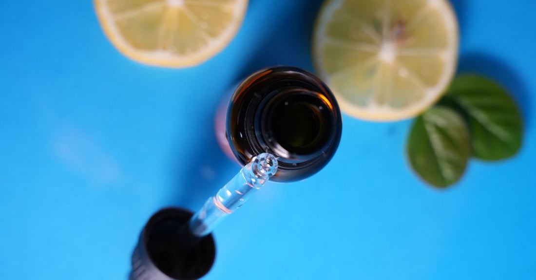 A clear glass dropper bottle of vitamin C serum on a light marble surface, symbolising vitamin C serum benefits for brighter, firmer skin.