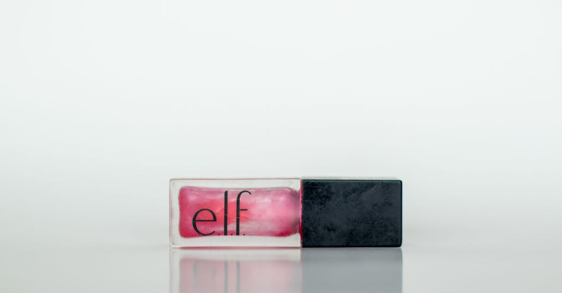 A clear lip gloss tube with a plumping wand applicator resting on a reflective surface, representing the best lip gloss for plump lips UK shoppers seek.