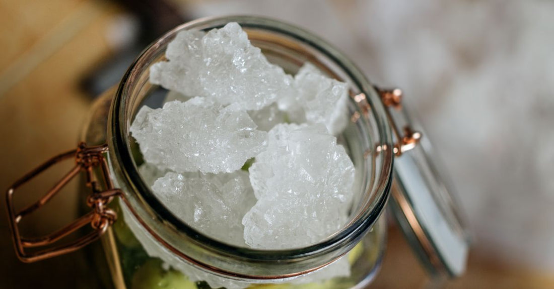 A jar of natural sugar scrub with wooden spoon on a bathroom shelf, illustrating the scrubs buying guide UK.