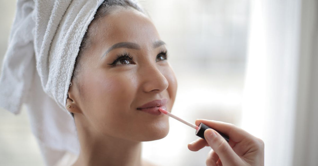 A clear lip gloss tube with a doe-foot applicator resting on a marble surface, representing the best lip gloss for plump lips.