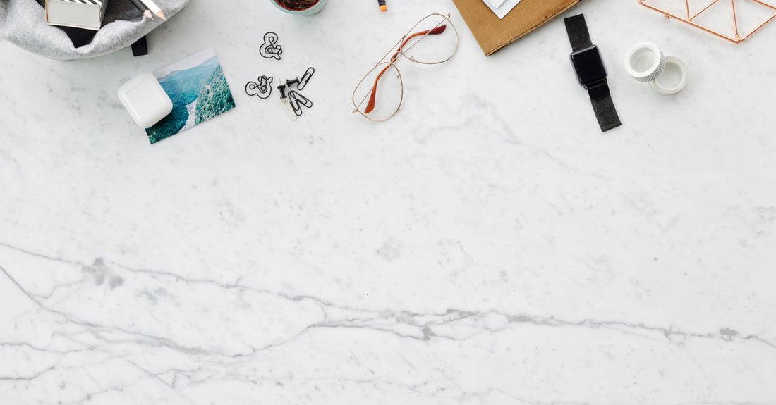 A flatlay of quality bath and bathing accessories including salts, oils and a loofah on a marble surface.