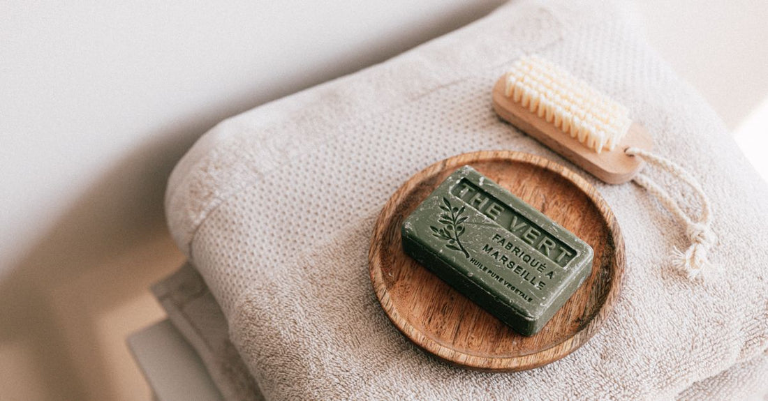 A flatlay of the best bath & bathing accessories UK 2026 including a loofah, brush, and oils on a marble surface.