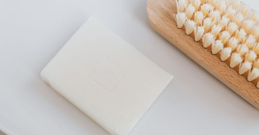 A set of wooden-handled nail cleaning brushes with dual-sided soft and stiff bristles, laid on a white marble surface with a towel.