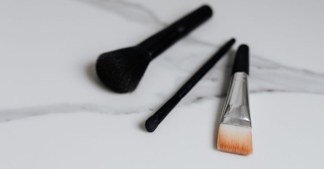 A collection of bath & body brushes on a light marble surface, showing different bristle types and handle designs, as featured in the Avelisse buying guide.