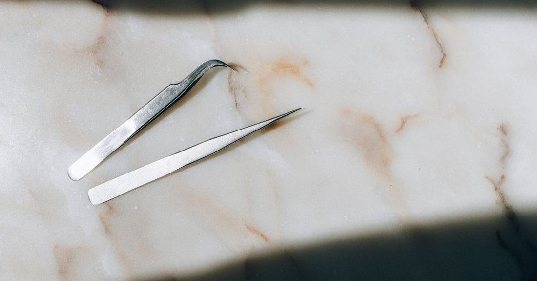 A pair of natural-looking false eyelashes lying on a white surface next to lash glue and tweezers, demonstrating how to apply false lashes.