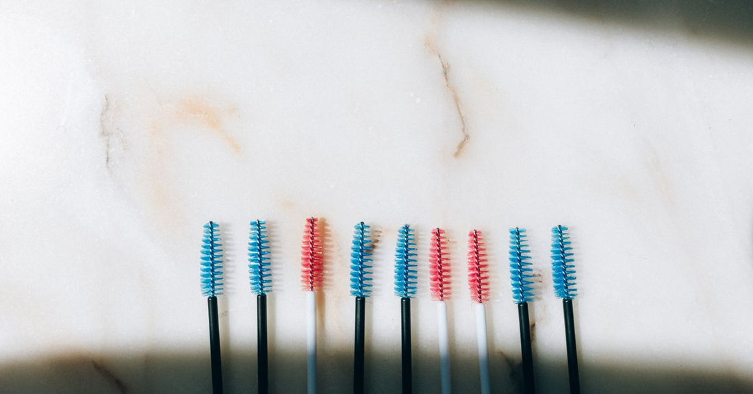 Best eyelash adhesives 2026: three eyelash glue bottles on a marble surface with a lash applicator.