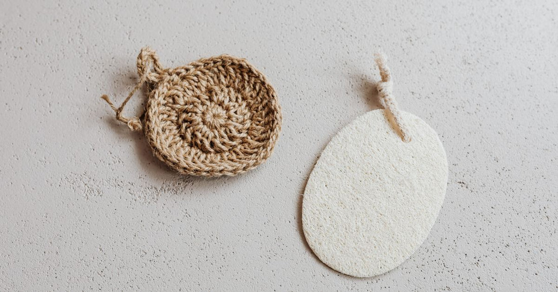A collection of natural bath sponges including a loofah, konjac sponge, and mesh pouf on a bathroom shelf, illustrating a bath sponges buying guide