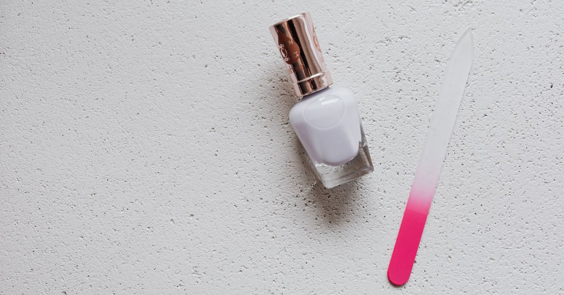 A clear glass bottle of nail strengthener on a white marble surface, representing how to use nail strengthener for brittle nails.