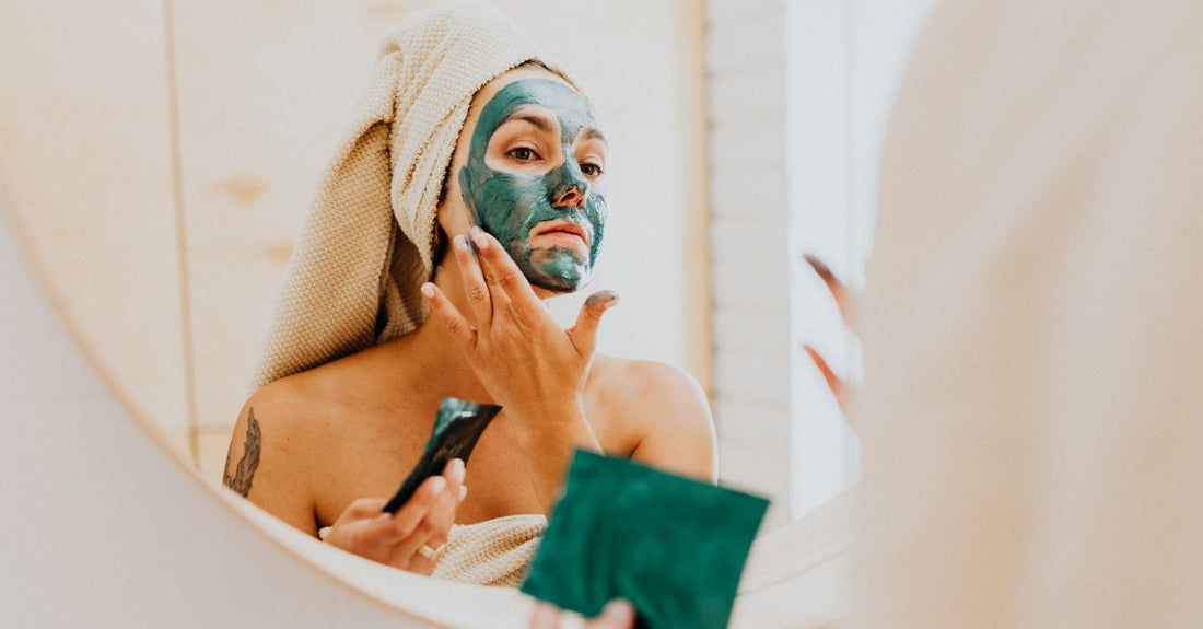 A selection of summer skincare masks including a clay mask jar and sheet masks, arranged on a light surface with tropical green leaves.