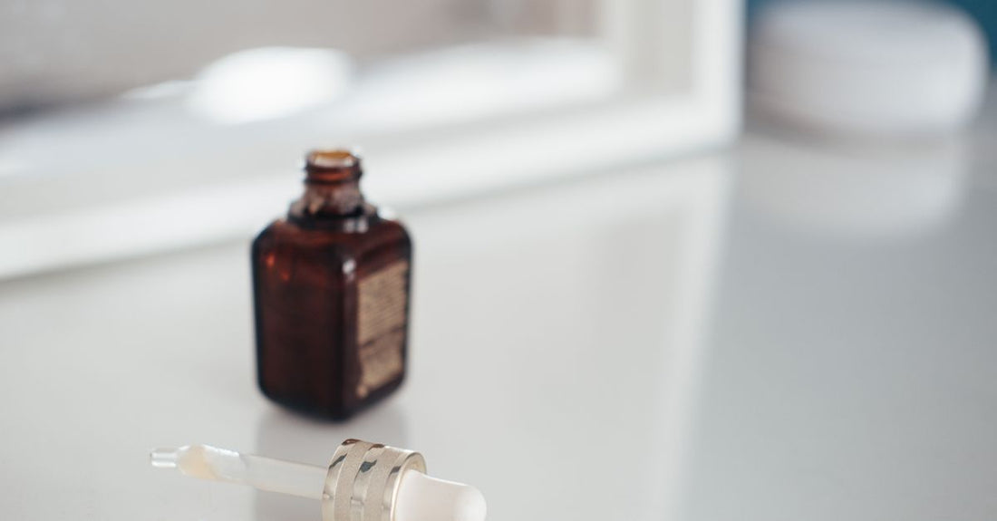 A collection of neck and décolleté skincare products in glass bottles and jars on a marble surface, representing a neck & décolleté buying guide UK.