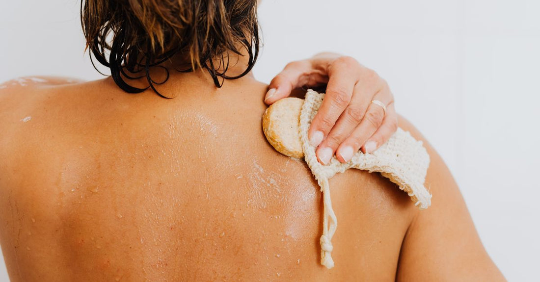 A collection of natural bath sponges and loofahs on a bathroom shelf, illustrating a bathing buying guide for softer skin.