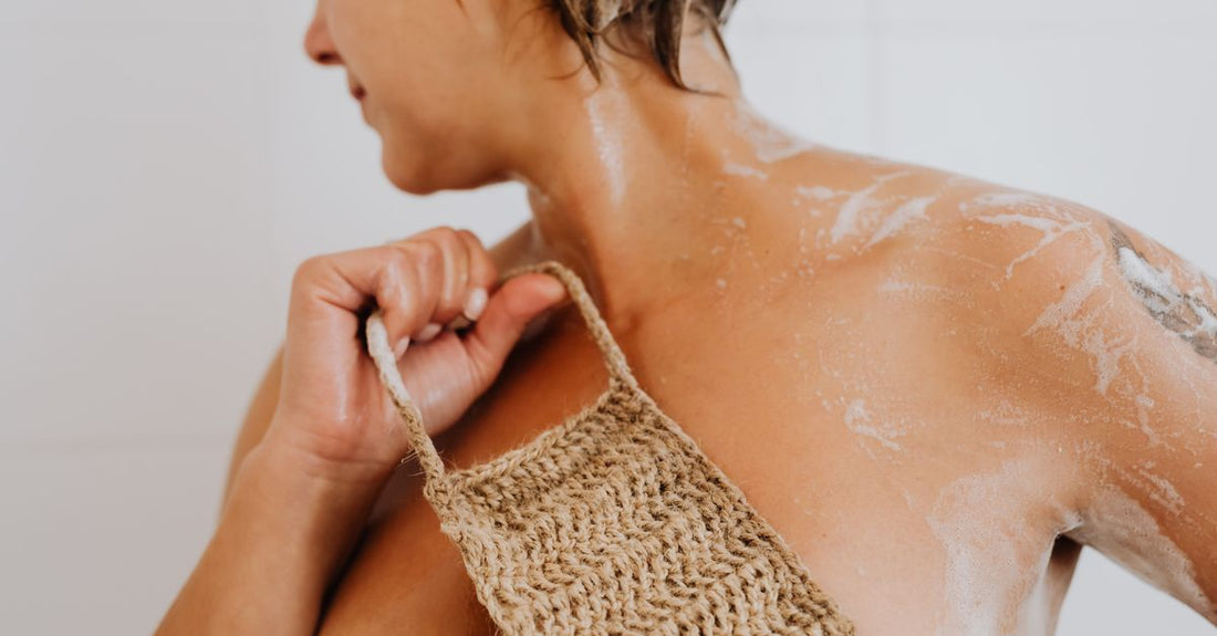 A natural loofah pad and sea sponge on a bathroom shelf, illustrating the best bathing accessories 2026 for exfoliation.