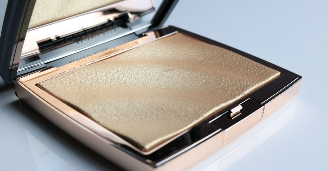 Close-up of a shimmering highlighter compact on a white marble surface, illustrating the highlighters & luminizers buying guide UK.