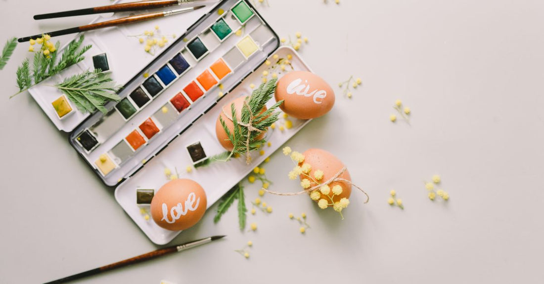 Body paint buying guide showcasing a flatlay of colourful water-based body paint palettes and brushes on a white surface.