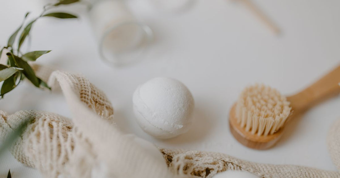 A flatlay of bath & bathing accessories including a natural sea sponge, bamboo back brush, and bath pillow on a marble surface, illustrating the bath & bathing accessories buying guide UK.