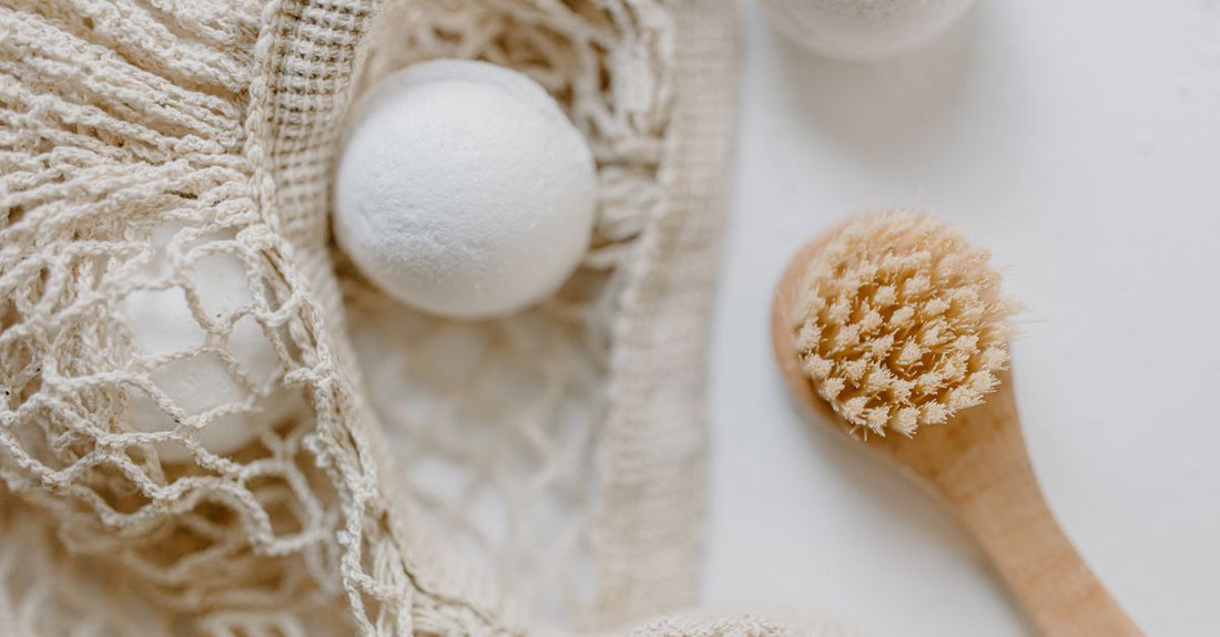 A flatlay of various bath and body brushes including a long-handled back scrubber, a dry brush, and a silicone body scrubber, demonstrating how to choose bath & body brushes for exfoliation.