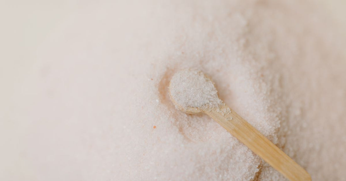 Three glass jars of natural bath salts — Epsom, Dead Sea and Himalayan pink — on a wooden shelf, illustrating a bath salts buying guide.