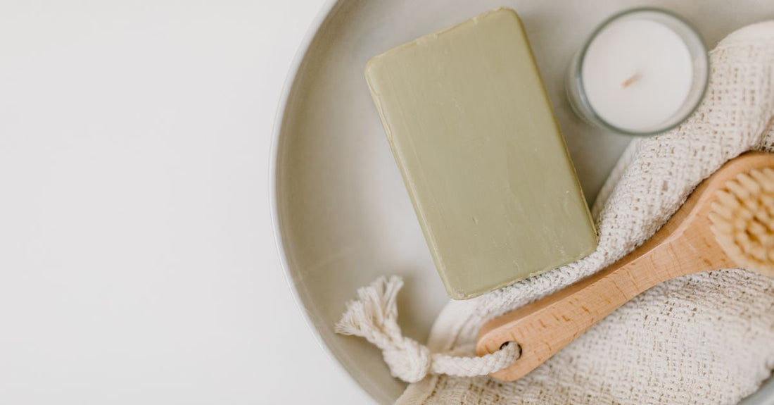 A selection of bath and bathing accessories including salts, oils, and a loofah arranged on a spa-style bathroom shelf, illustrating how to choose bath & bathing accessories.