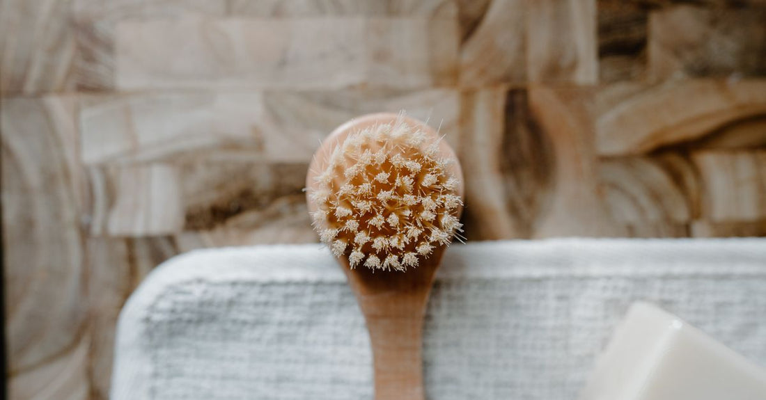 A flatlay of wooden bath and body brushes with natural bristles, a loofah, and a long-handled back scrubber on a white background.