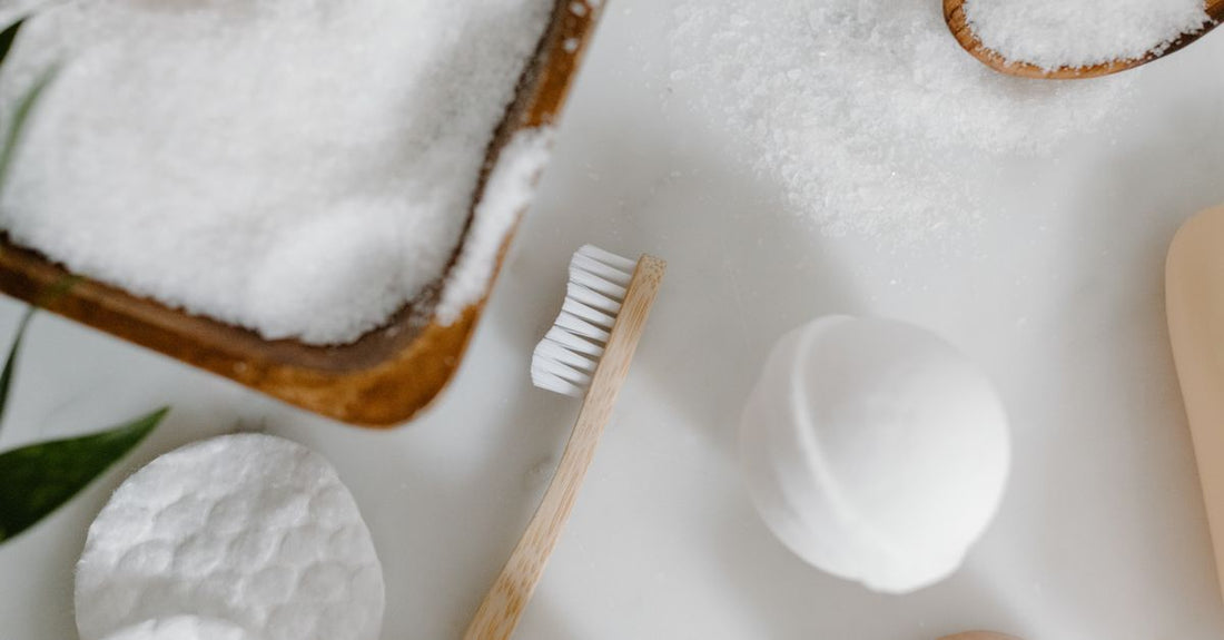 A flat lay of various bathing accessories including a wooden bath brush, exfoliating gloves, and a natural loofah on a marble surface.