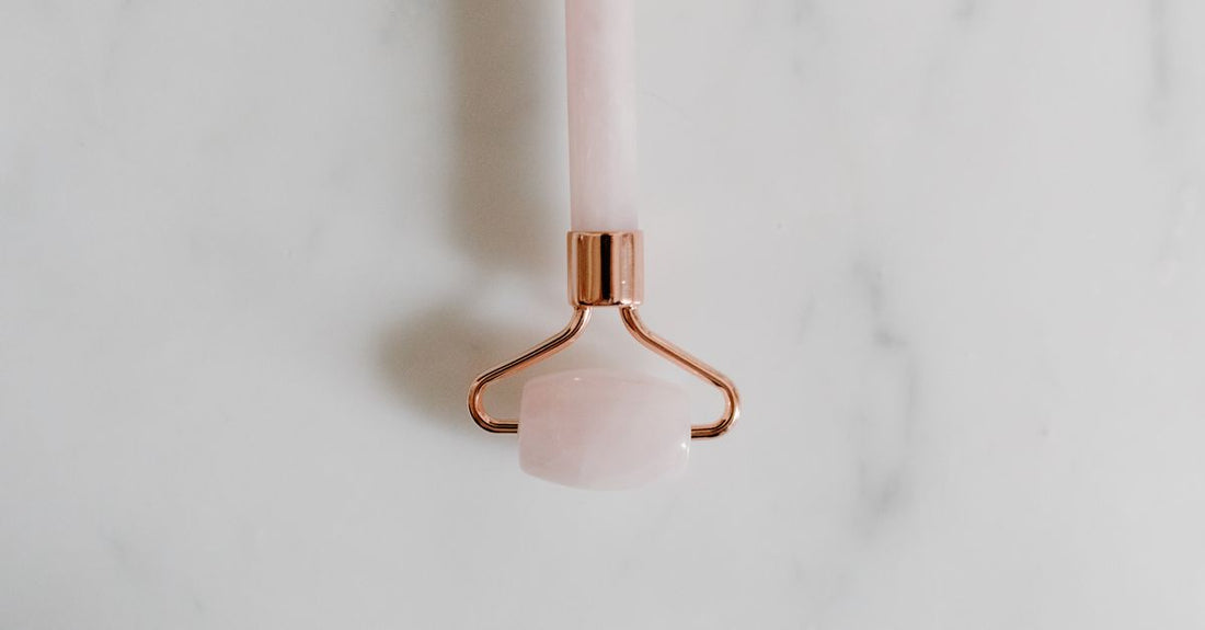 A flatlay of various facial rollers including jade, rose quartz, and metal options on a marble surface, illustrating a facial rollers buying guide.