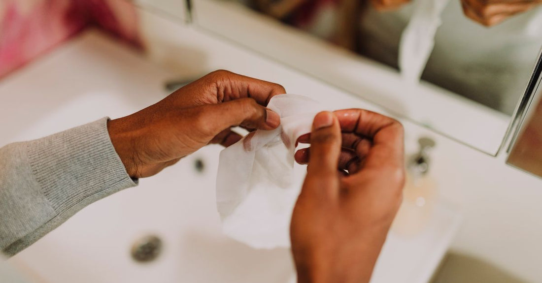 A stack of soft microfibre cleansing cloths and a jar of exfoliating towelettes on a bathroom shelf, illustrating how to choose cloths & towelettes.