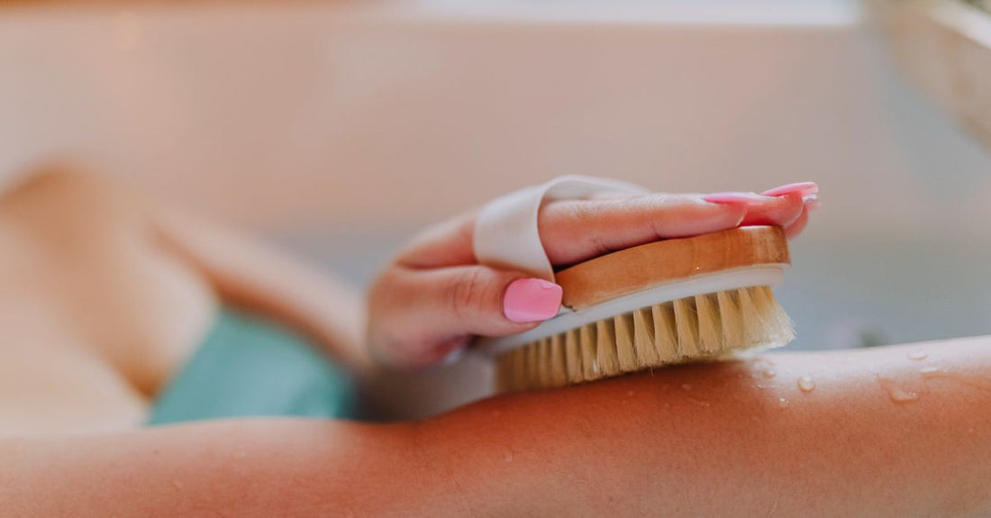 A set of natural bristle bath and body brushes arranged on a white towel, including a long-handled back brush and a dry body brush.