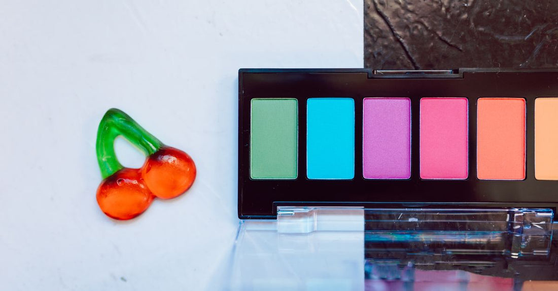 A flatlay of a concealer and neutralizer palette with six colour-correcting shades, a makeup brush, and a marble background.