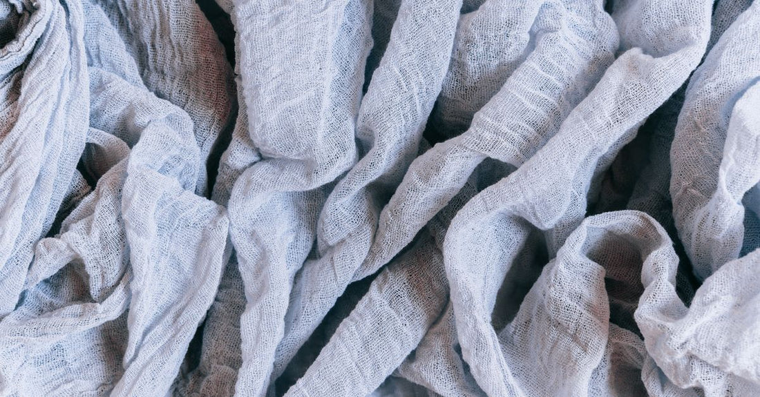 Stack of soft cotton muslin cloths and biodegradable facial towelettes arranged on a neutral surface, illustrating how to choose cloths & towelettes for different skincare needs.