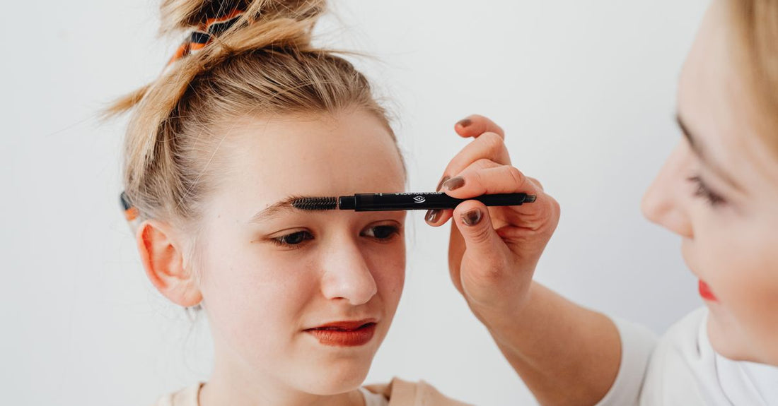 Angled brow brush and spoolie flatlay on a white marble surface, part of a brow brushes buying guide.