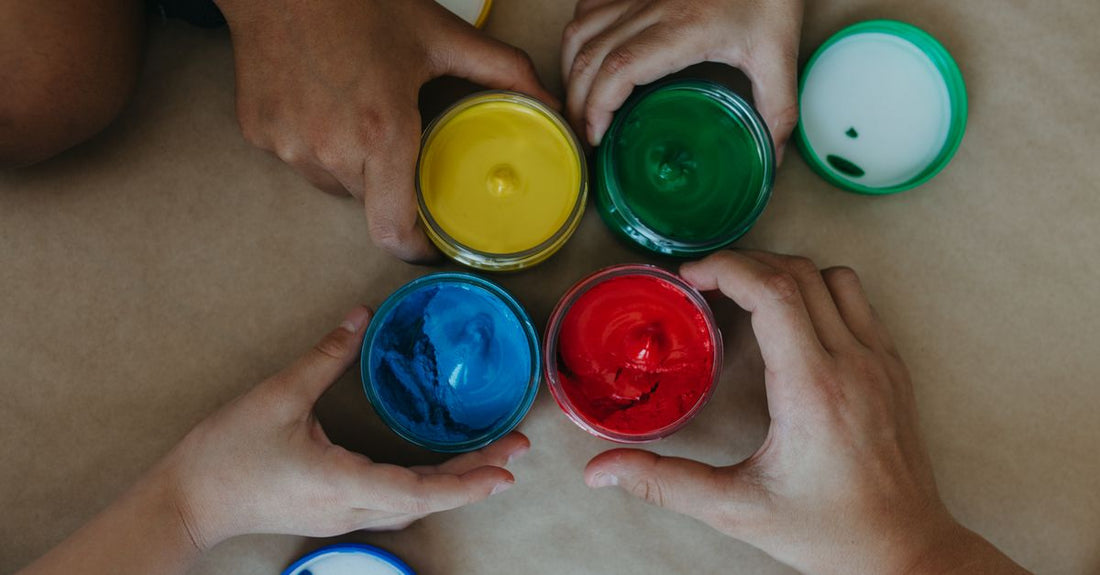 A flatlay of colourful body paint pots and brushes on a white surface, illustrating the best body paint 2026 options for seamless routine integration.