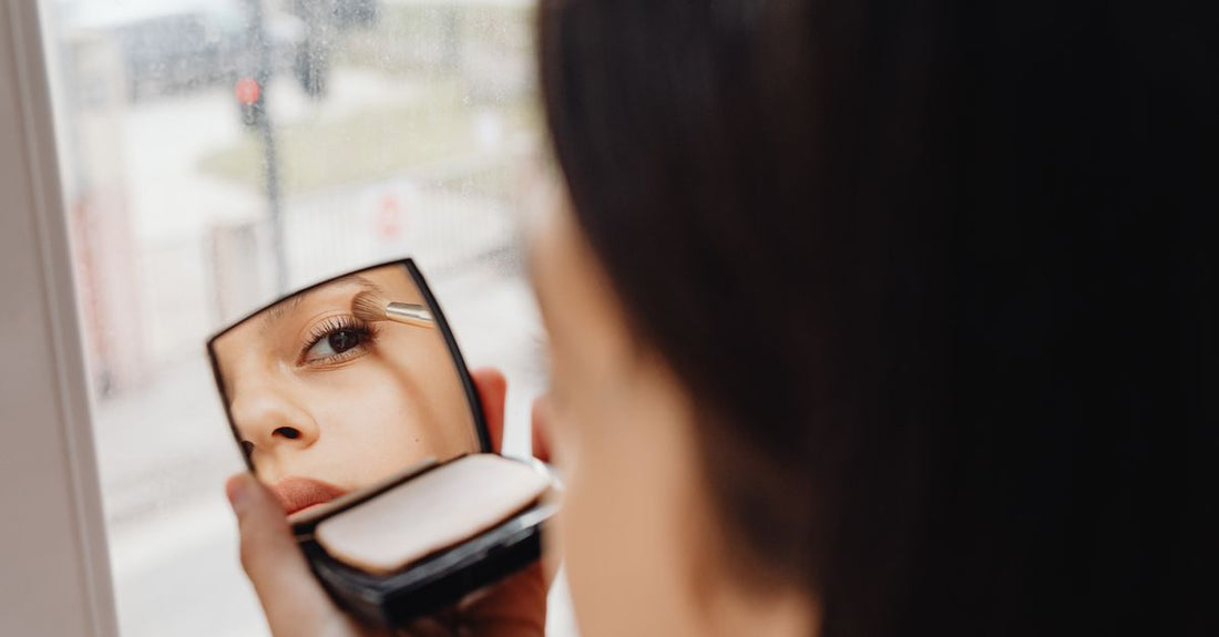 A sleek compact travel mirror with LED lights and multiple magnification panels, open on a dressing table with makeup brushes visible, illustrating how to choose compact & travel mirrors for British beauty routines.