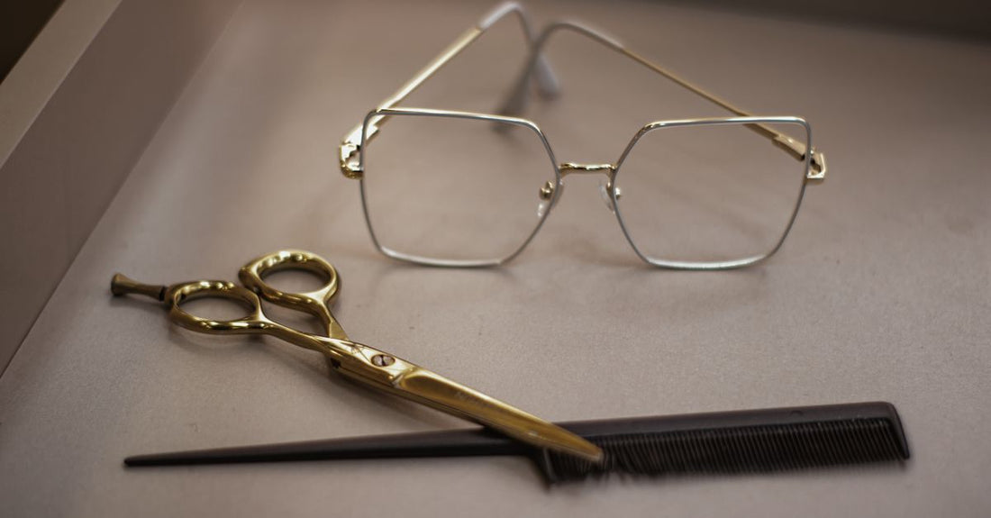 Pair of precision eyebrow scissors resting on a white marble surface, showing curved stainless steel blades and ergonomic handles for safe at-home brow grooming.