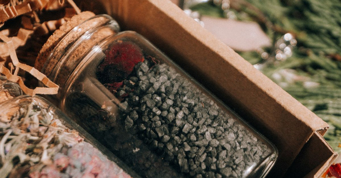 An assortment of bath salts in glass jars alongside a wooden scoop on a marble surface, illustrating how to choose bath salts for gifting.