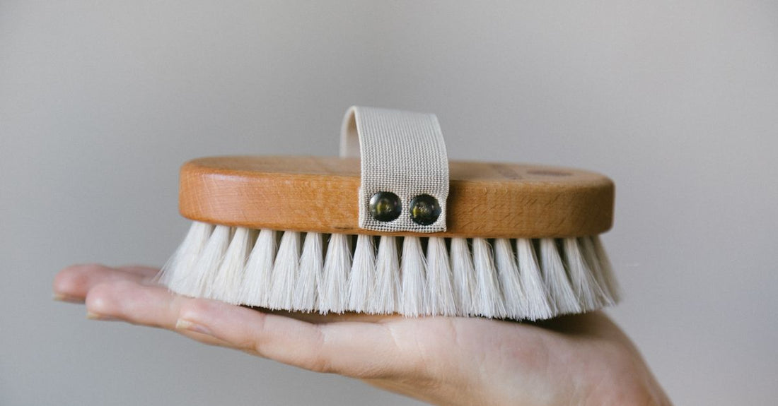 Natural bristle bath and body brush with wooden handle on a white bathroom shelf.