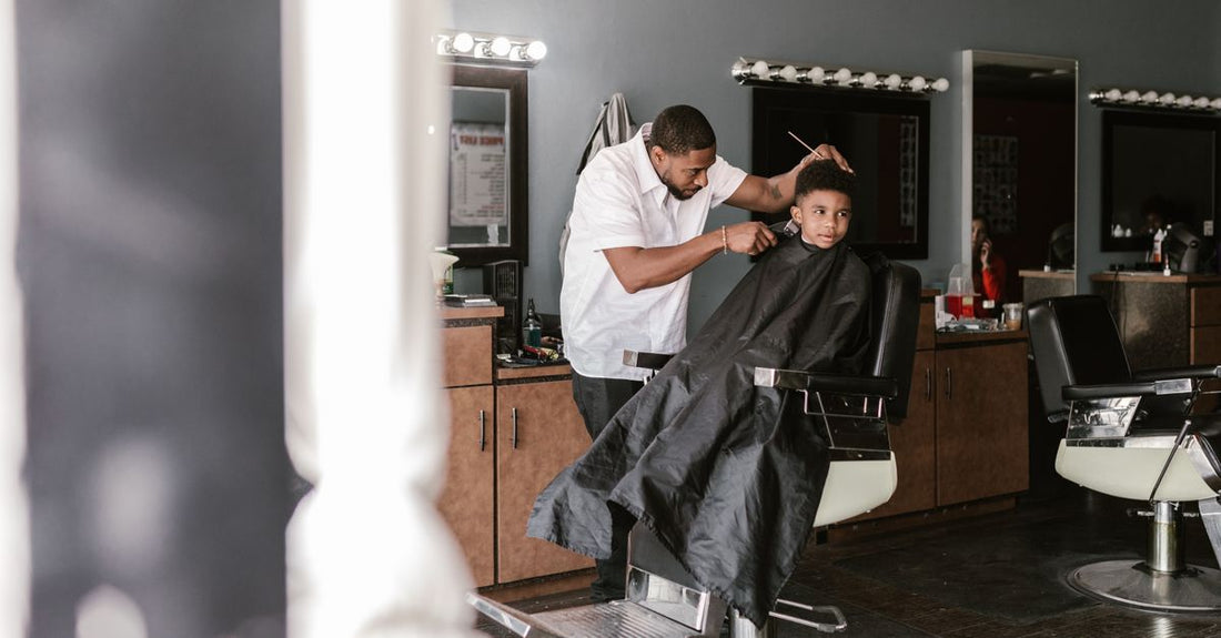 A black waterproof salon cape laid flat on a white surface, showcasing snap closure and sleek design, representing the best capes 2026.