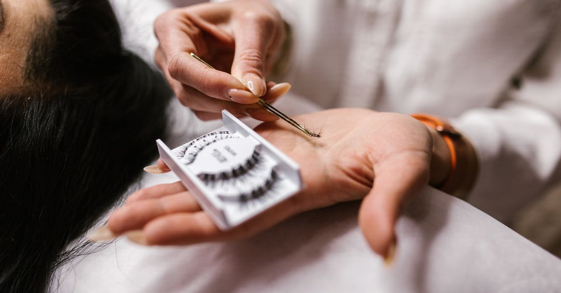 A pair of false eyelash strips with a tube of lash glue on a clean white marble surface, demonstrating how to apply false lashes with glue.