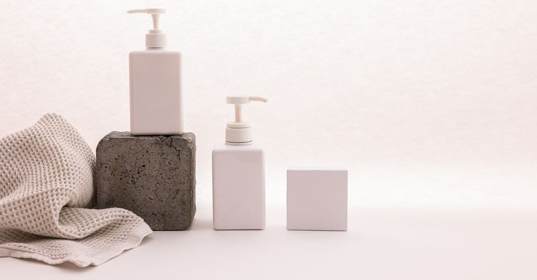 A flatlay of self-tanning bottles and mitts on a white surface, illustrating how to choose body self-tanners for different skin types.