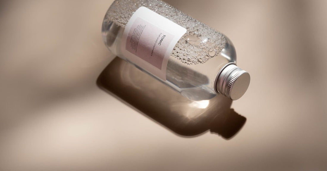 A glass bottle of best hair tonics UK 2026 on a marble surface with fresh rosemary sprigs.