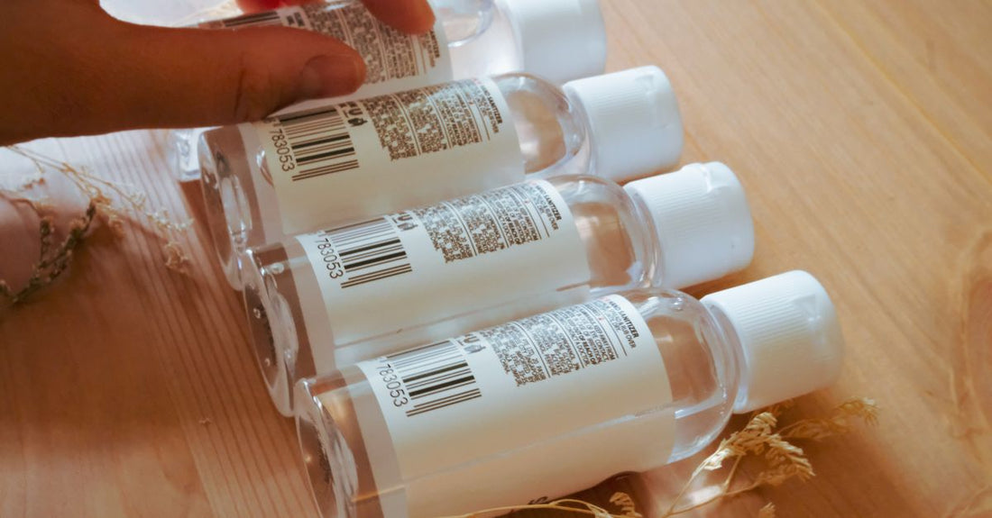 A row of transparent micellar water bottles on a white marble surface, showcasing a makeup cleansing water buying guide theme.