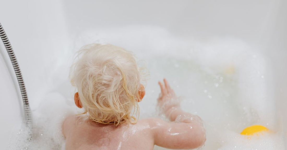 Baby bubble bath bottle on a white shelf beside a soft towel, illustrating a baby bubble bath & cleansers buying guide UK.